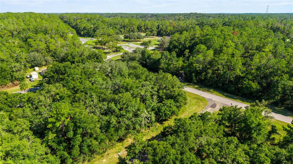 An aerial view shows a wooded lot bordered by paved roads and nearby residential structures — 11023 N GLENDA TERRACE, DUNNELLON, FL