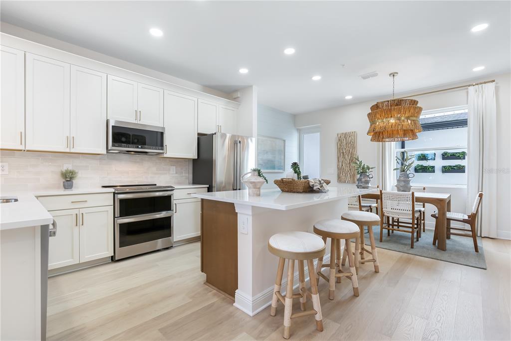 A modern kitchen features white cabinetry, a central island with bar stools, and dining area — 17812 BROADLEAF LOOP, VENICE, FL