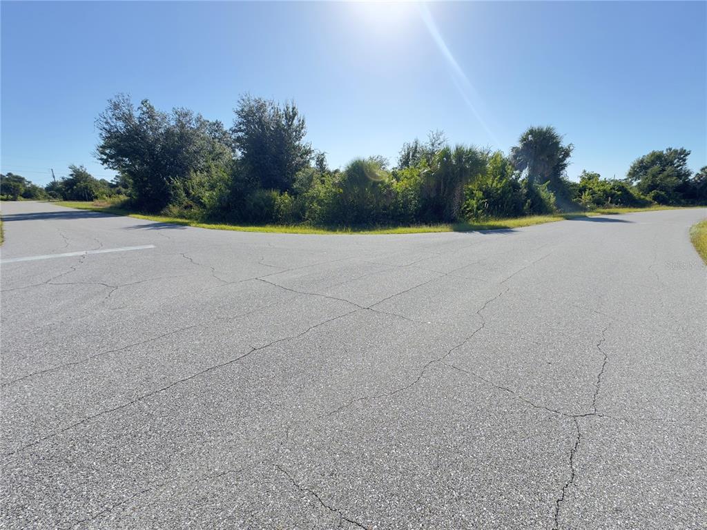 An asphalt road intersection meets a vacant, overgrown lot under a bright sun — 13125 REVELL LANE, PORT CHARLOTTE, FL