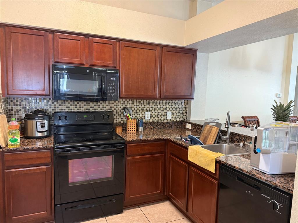 A kitchen features dark wood cabinets, granite countertops, a mosaic tile backsplash, and black appliances — 18250 SNOWDONIA DRIVE, LAND O LAKES, FL