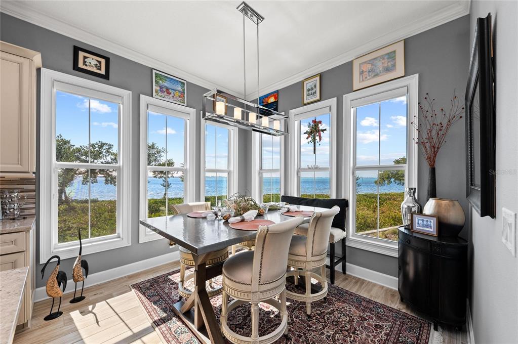 A dining area features a metal table, upholstered chairs, and large windows overlooking the water — 268 SAINT LUCIA DRIVE UNIT 101, BRADENTON, FL