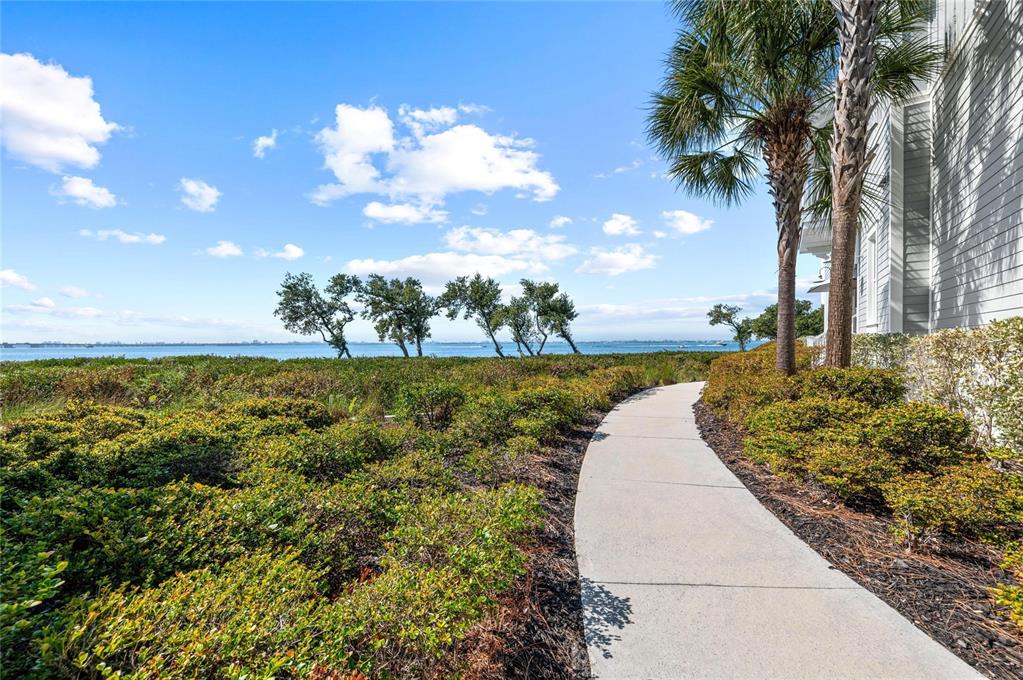 A concrete walkway winds through coastal landscaping toward a view of the water — 268 SAINT LUCIA DRIVE UNIT 101, BRADENTON, FL