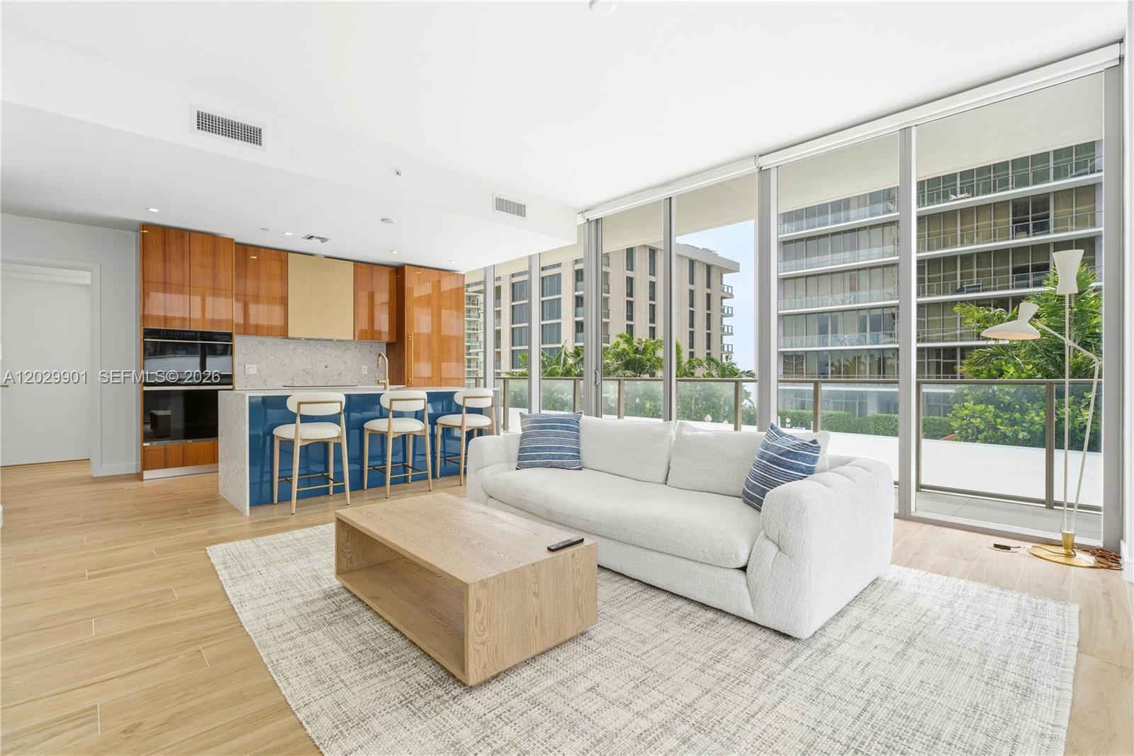 A modern living room features a blue kitchen island, white sofa, and floor-to-ceiling windows — 2678 Tigertail Ave # 911, Miami FL 33133, MIAMI, FL