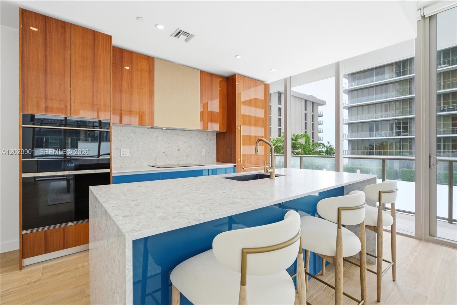 A modern kitchen features blue cabinetry, wood-toned upper cabinets, a stone island, and floor-to-ceiling windows — 2678 Tigertail Ave # 911, Miami FL 33133, MIAMI, FL