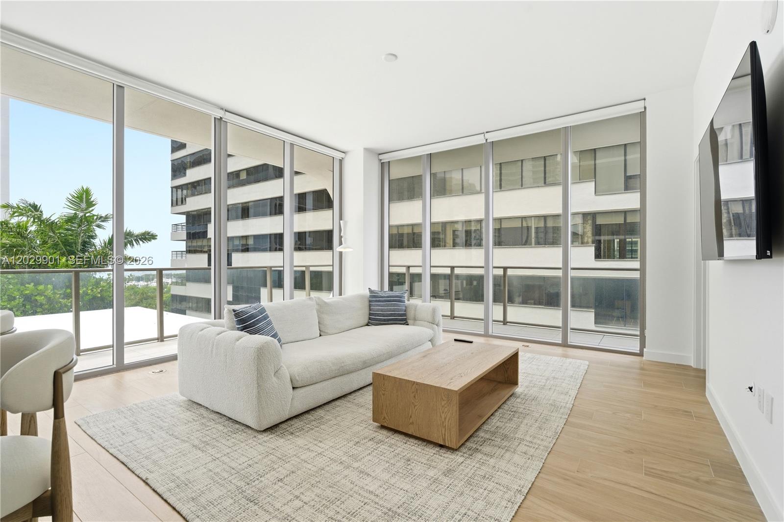 A modern living room features a white sofa, wooden coffee table, and floor-to-ceiling windows — 2678 Tigertail Ave # 911, Miami FL 33133, MIAMI, FL