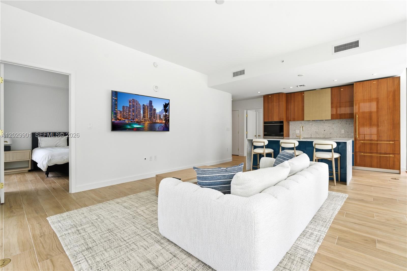 A modern living room features a white sofa, wall-mounted television, and an open kitchen area — 2678 Tigertail Ave # 911, Miami FL 33133, MIAMI, FL