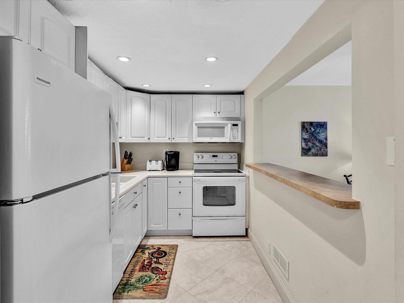 A galley-style kitchen features white cabinets, white appliances, and a pass-through window with a counter — 1421 S Ocean Boulevard # 219, Pompano Beach FL 33062, POMPANO BEACH, FL