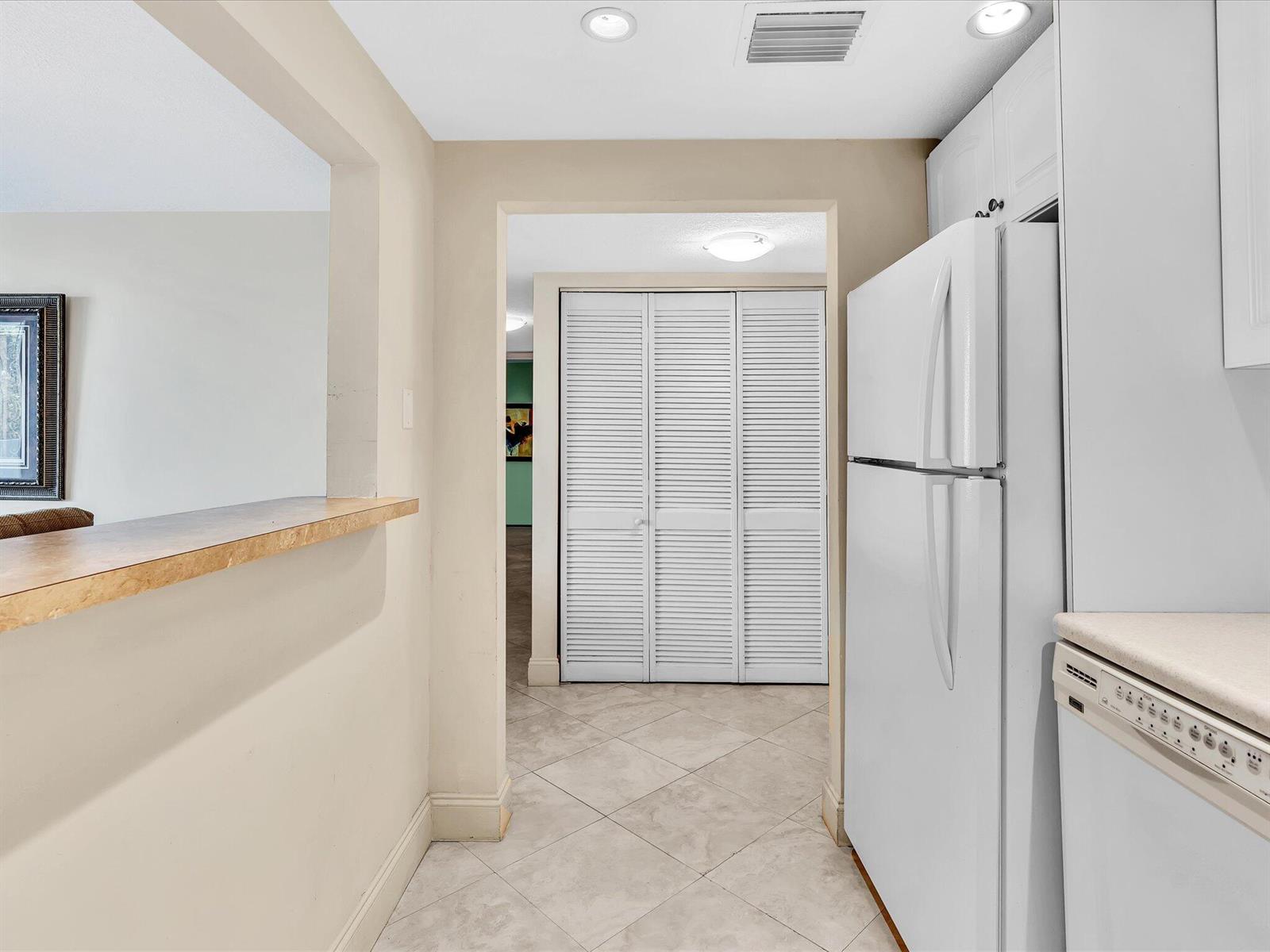 A kitchen with a breakfast bar, white appliances, and a tiled floor leading to a hallway — 1421 S Ocean Boulevard # 219, Pompano Beach FL 33062, POMPANO BEACH, FL