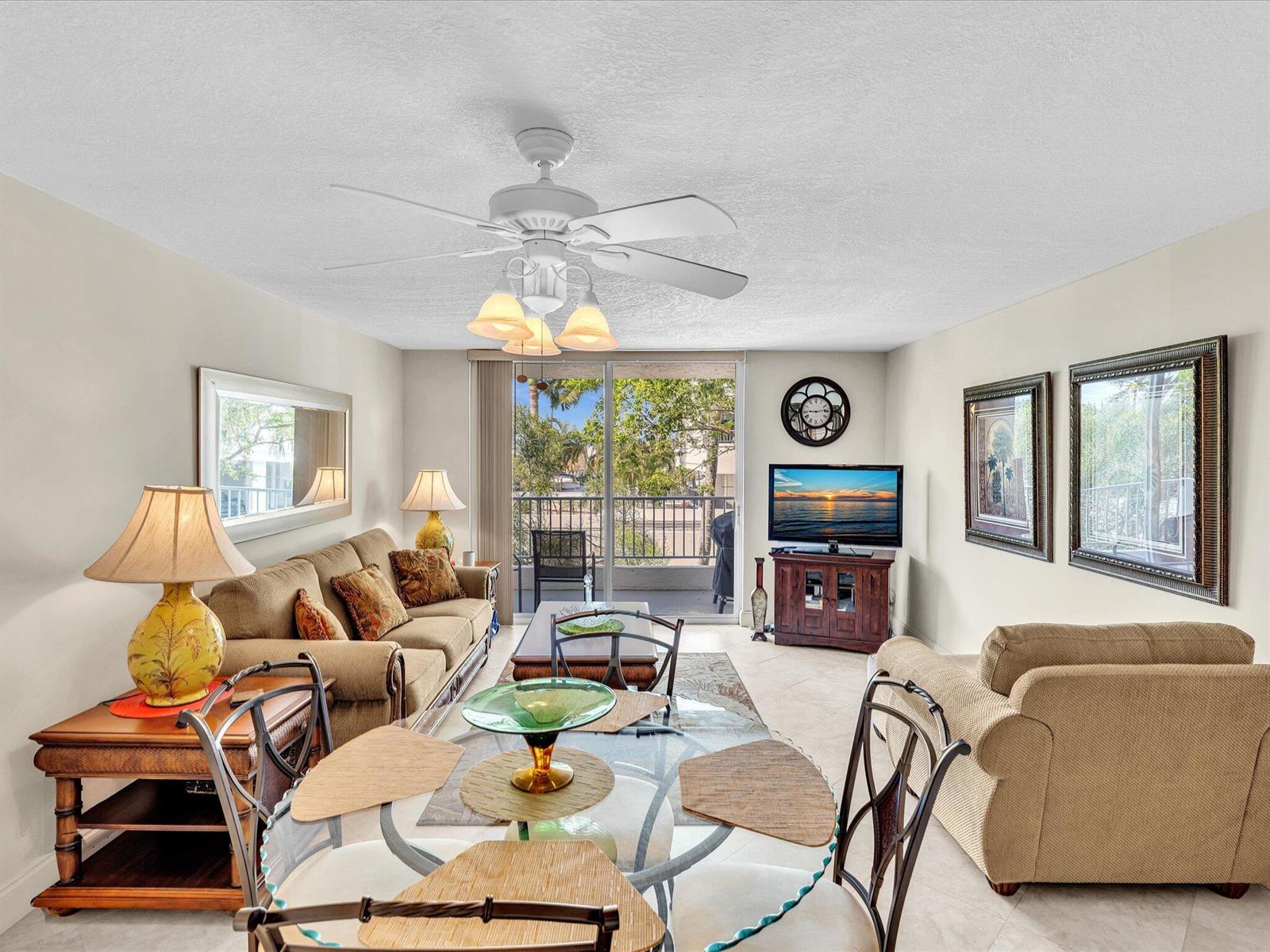 A living room with a glass dining table, beige sofa, ceiling fan, and balcony access — 1421 S Ocean Boulevard # 219, Pompano Beach FL 33062, POMPANO BEACH, FL