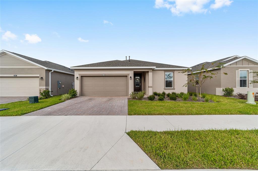 A single-story suburban house with a tan stucco exterior, a two-car garage, and a driveway — 5521 NW 45TH LANE, OCALA, FL