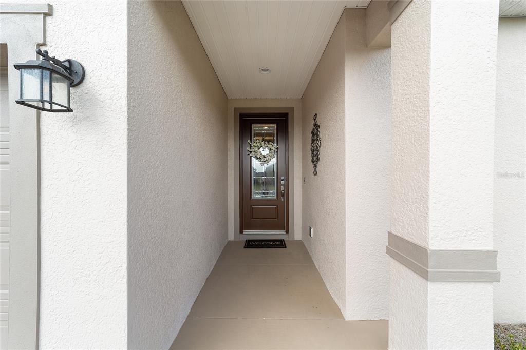 A covered entryway features a brown front door with a glass insert and a welcome mat — 5521 NW 45TH LANE, OCALA, FL