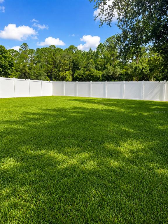 A large, grassy backyard enclosed by a white vinyl privacy fence with trees in the background — 29 HERRING COURT, POINCIANA, FL