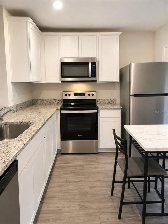 A kitchen features white cabinets, granite countertops, stainless steel appliances, and wood-look flooring — 29 HERRING COURT, POINCIANA, FL