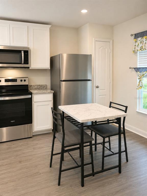 A kitchen features white cabinets, stainless steel appliances, a small dining table, and wood-look flooring — 29 HERRING COURT, POINCIANA, FL