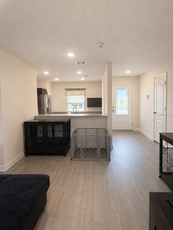 An open-concept kitchen and entryway feature light wood-look flooring and a dark pet crate — 29 HERRING COURT, POINCIANA, FL
