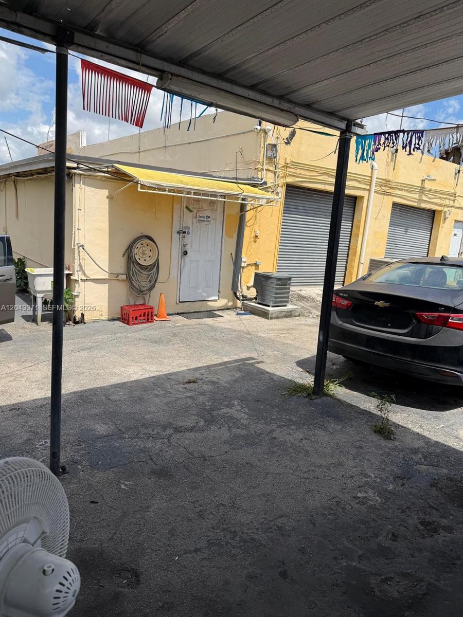An exterior view of a building with a yellow facade, metal roll-up doors, and parking — 3445 NW 27th Ave, Miami FL 33142, MIAMI, FL