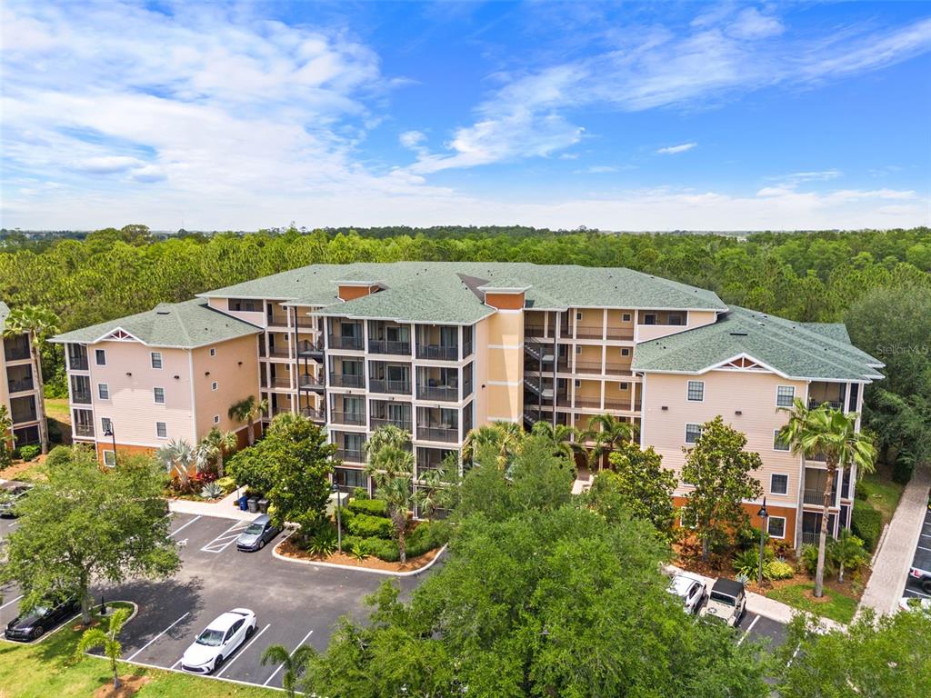 An aerial view of a multi-story apartment building with a parking lot and surrounding trees — 3060 PIRATES RETREAT COURT UNIT 309, KISSIMMEE, FL