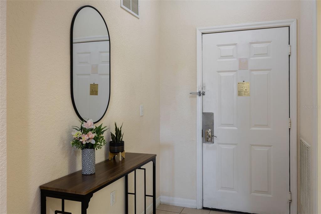 An entryway features a console table with a mirror, a plant, and a white door — 3060 PIRATES RETREAT COURT UNIT 309, KISSIMMEE, FL