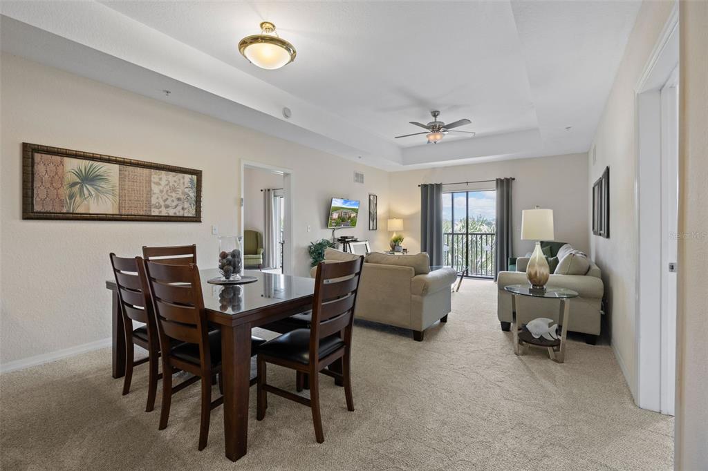 A dining area with a dark wood table and chairs opens into a carpeted living room — 3060 PIRATES RETREAT COURT UNIT 309, KISSIMMEE, FL