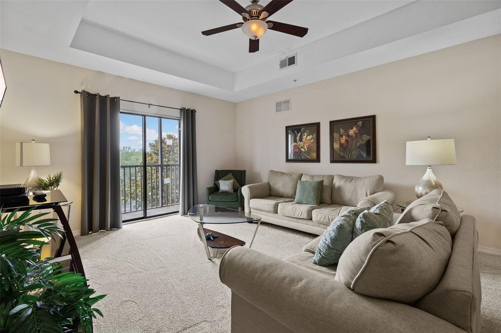 A living room features a tray ceiling, beige carpet, a sofa, and a sliding glass door — 3060 PIRATES RETREAT COURT UNIT 309, KISSIMMEE, FL