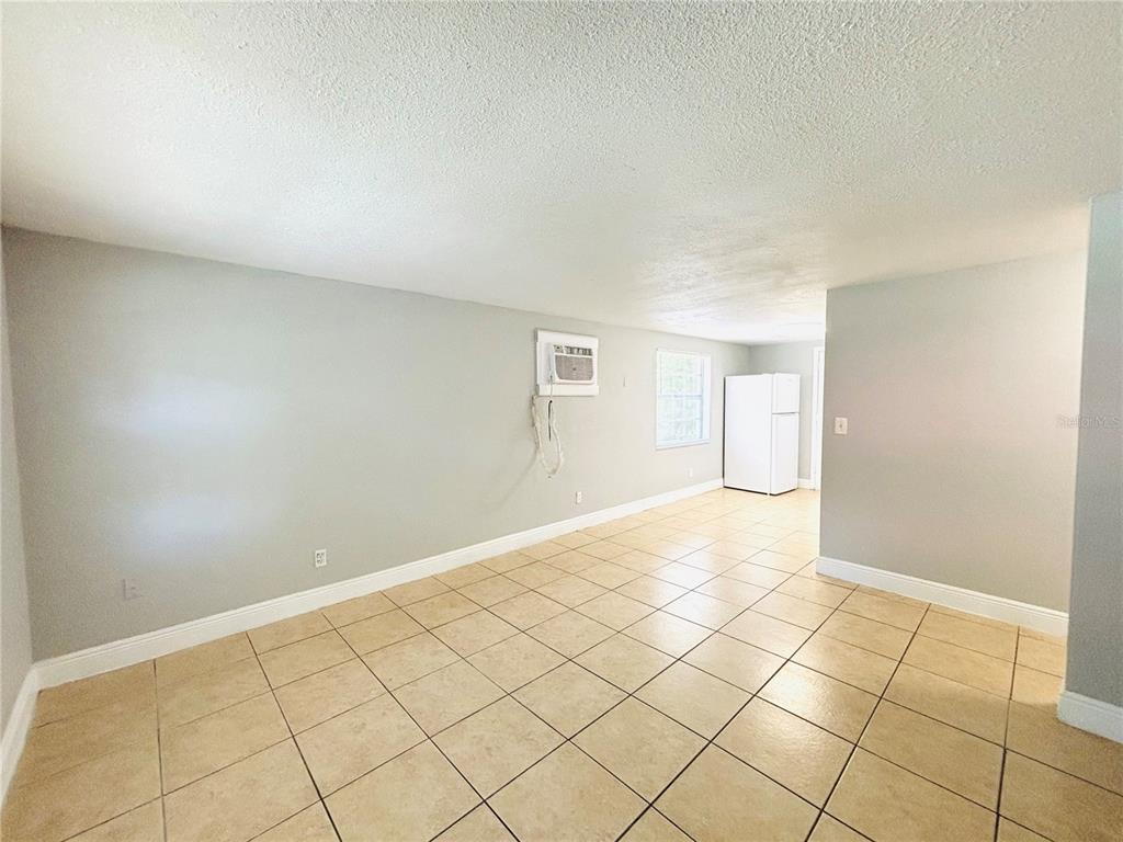 An interior view of a room with light gray walls, tan tile flooring, and a refrigerator — 11733 N 12TH STREET UNIT L, TAMPA, FL
