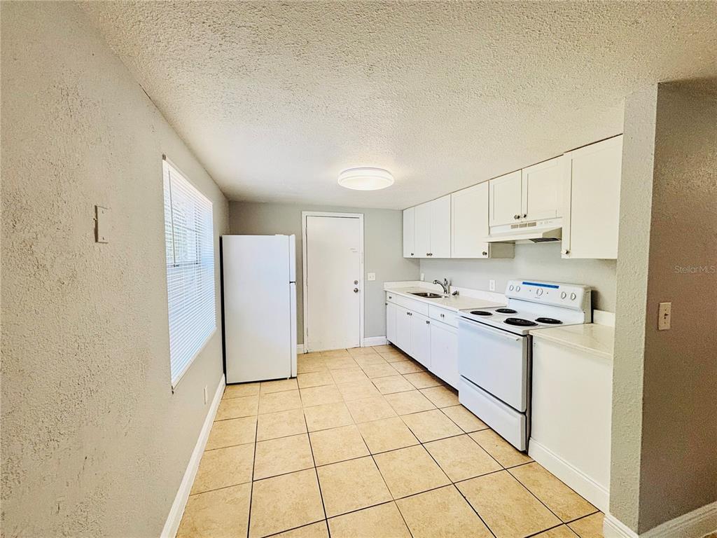 A kitchen features white cabinets, white appliances, and light-colored tile flooring — 11733 N 12TH STREET UNIT L, TAMPA, FL
