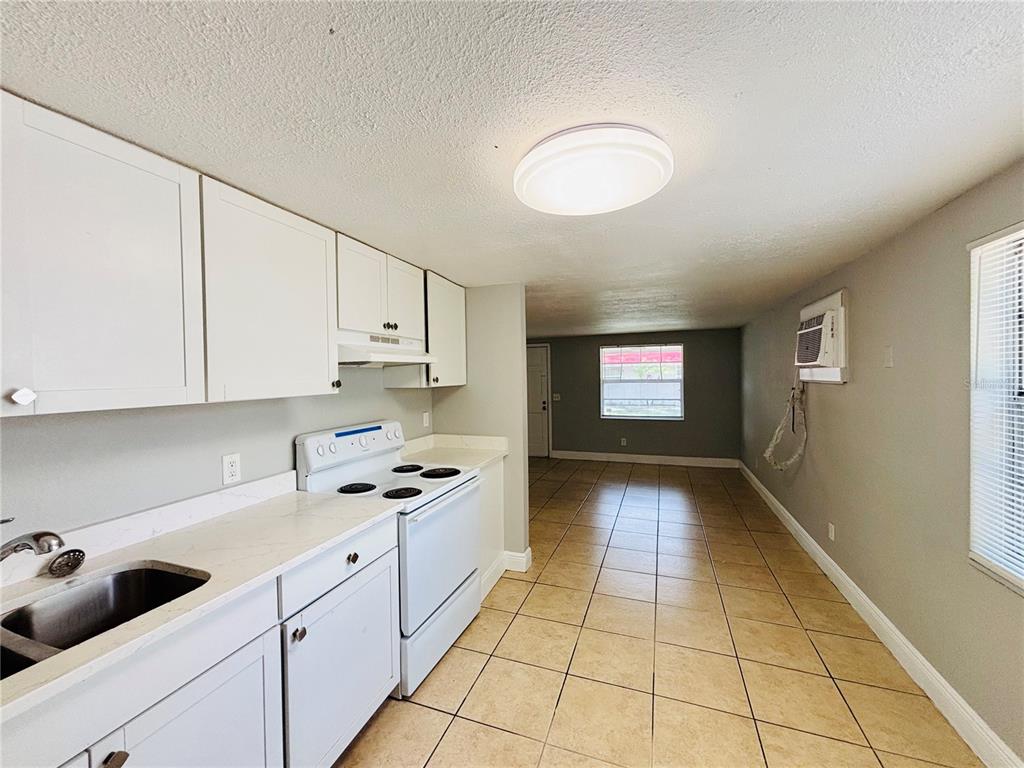 A kitchen with white cabinets and appliances features a sink, stove, and tiled flooring — 11733 N 12TH STREET UNIT L, TAMPA, FL