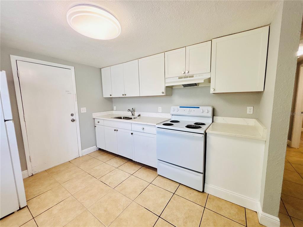 A kitchen features white cabinets, white appliances, a sink, and light-colored tile flooring — 11733 N 12TH STREET UNIT L, TAMPA, FL