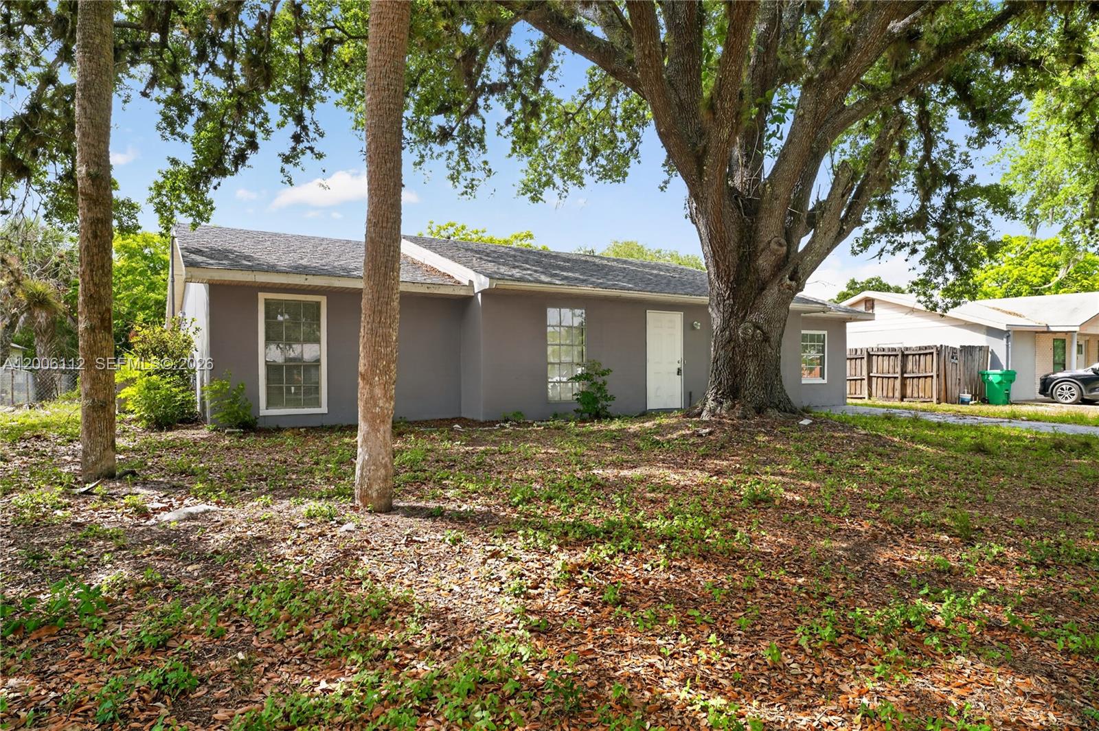 A gray single-story house sits on a lot with a large oak tree — 4030 SCHOOL CIR, La Belle FL 33935, LA BELLE, FL