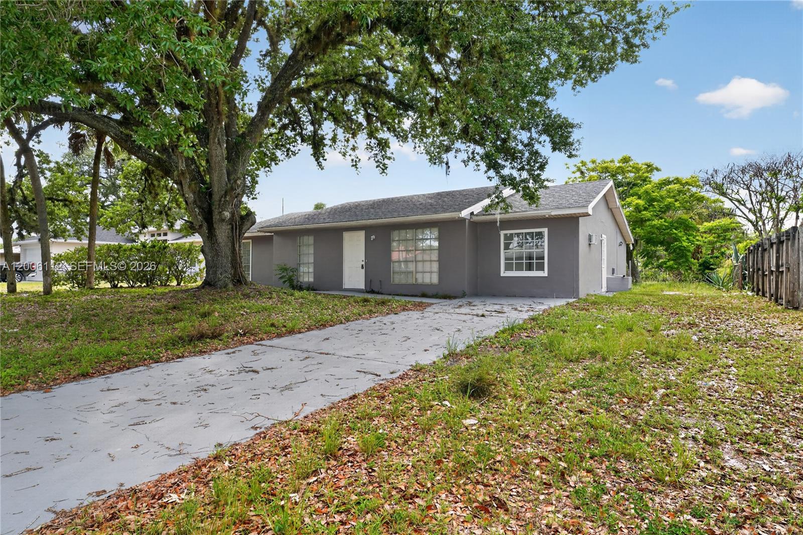 A gray, single-story house with a concrete driveway sits beneath a large, mature tree — 4030 SCHOOL CIR, La Belle FL 33935, LA BELLE, FL