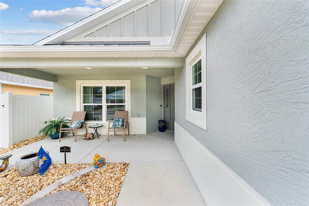 A covered front porch features two chairs, a small table, and decorative garden accents — 3463 LEELANAU COURT, THE VILLAGES, FL
