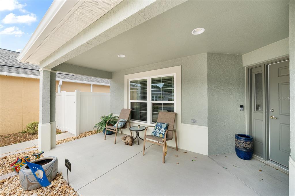 A covered concrete front porch features two chairs, a small table, and a front door — 3463 LEELANAU COURT, THE VILLAGES, FL