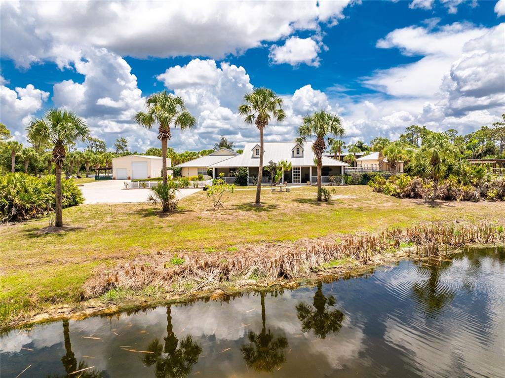 A white house with a metal roof sits behind a pond and palm trees — 668 PALOMINO TRAIL, ENGLEWOOD, FL