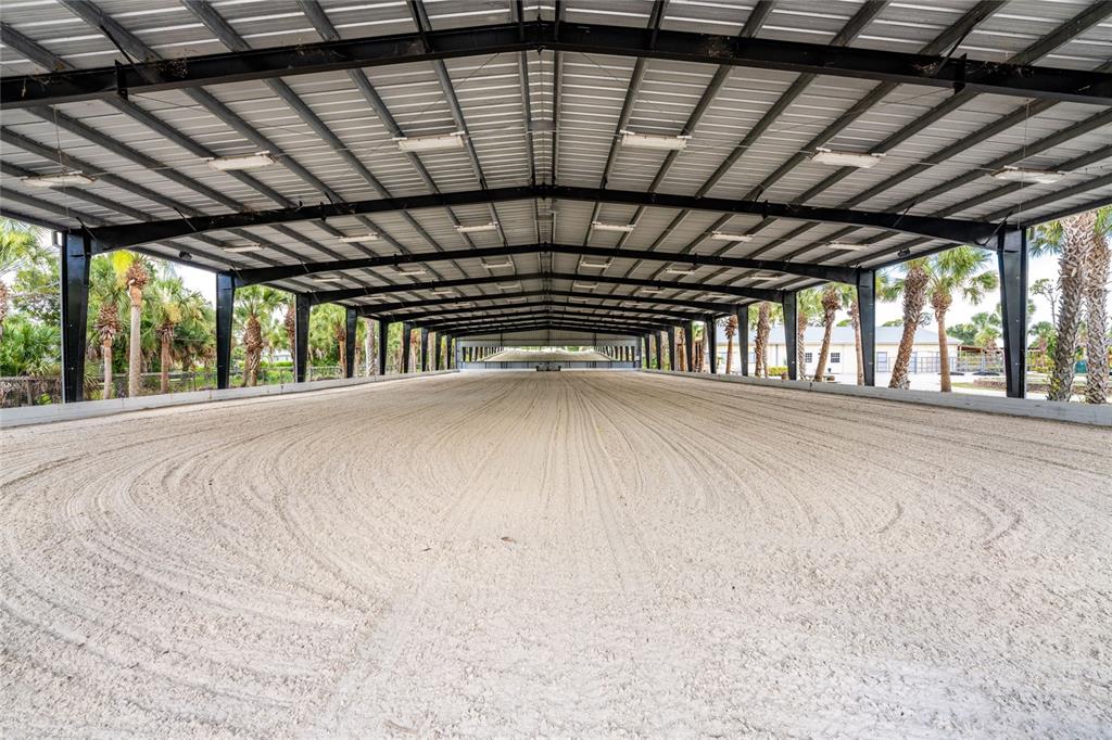A large, covered outdoor equestrian riding arena with a sand surface and metal frame structure — 668 PALOMINO TRAIL, ENGLEWOOD, FL