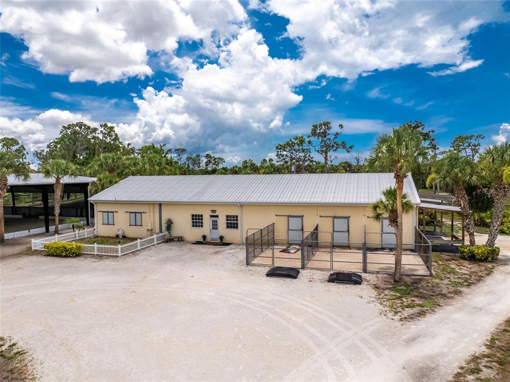 An exterior view of a tan building with a metal roof and outdoor animal enclosures — 668 PALOMINO TRAIL, ENGLEWOOD, FL