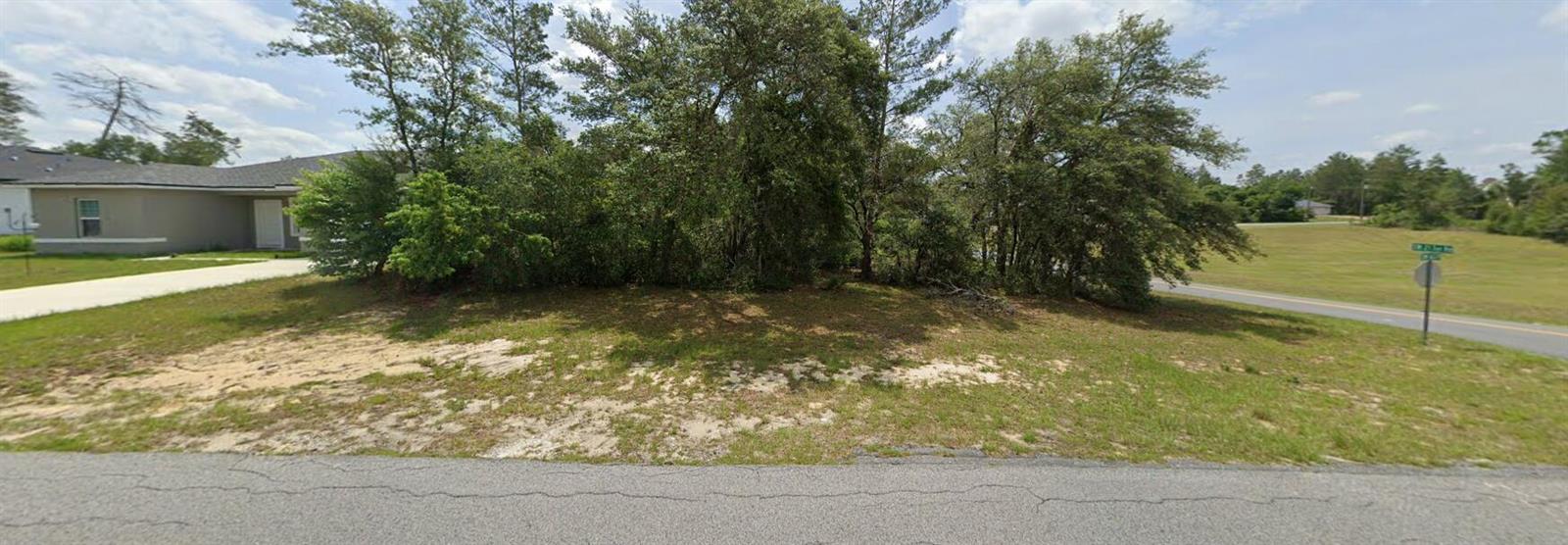 A vacant, grassy residential lot with trees sits between a house and a paved road — 2418 SW 163rd Place, Ocala FL 34473, OCALA, FL