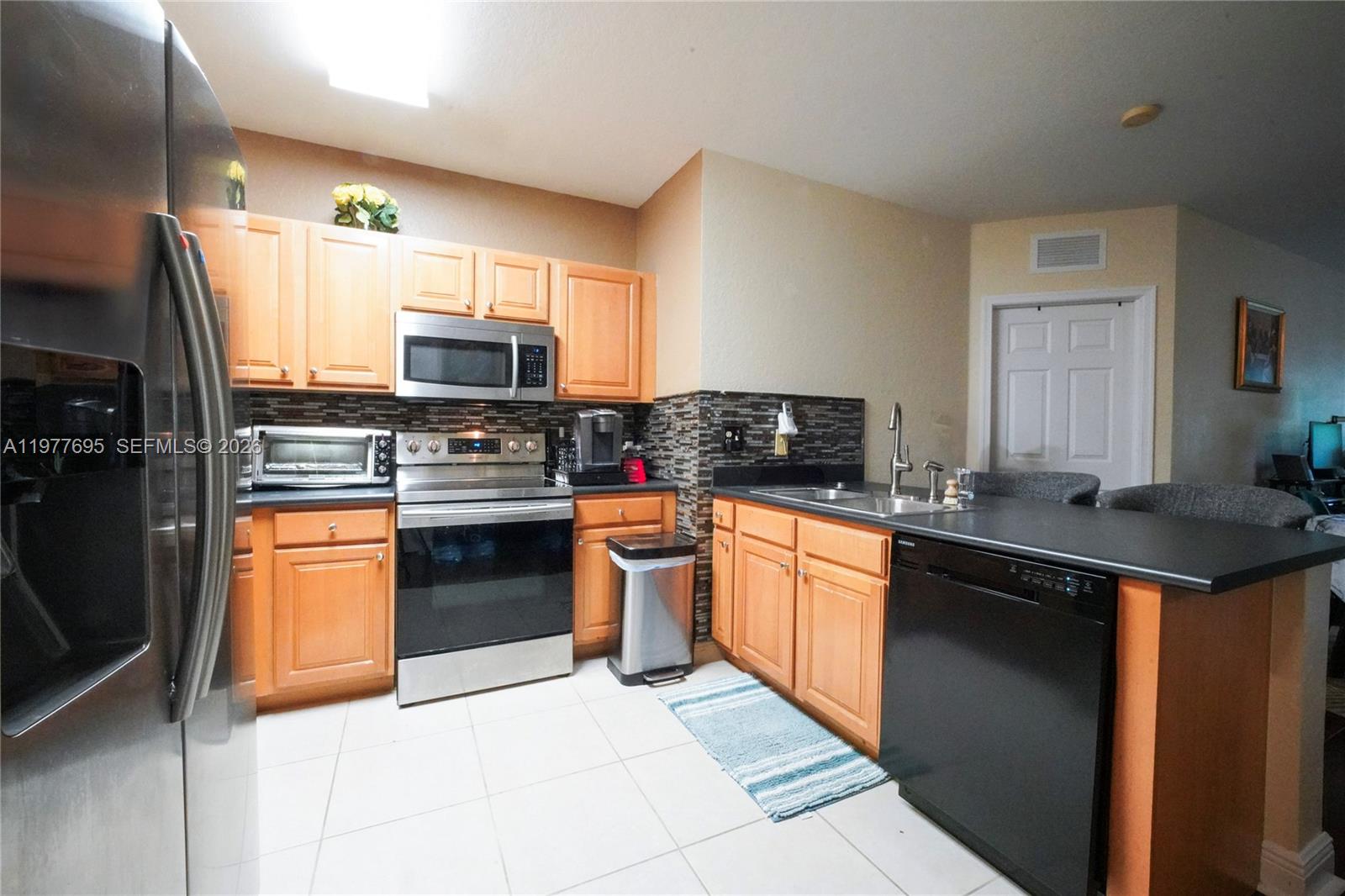 A kitchen features light wood cabinets, stainless steel appliances, dark countertops, and a tiled floor — 3335 Palomino Dr # 3, Davie FL 33024, DAVIE, FL