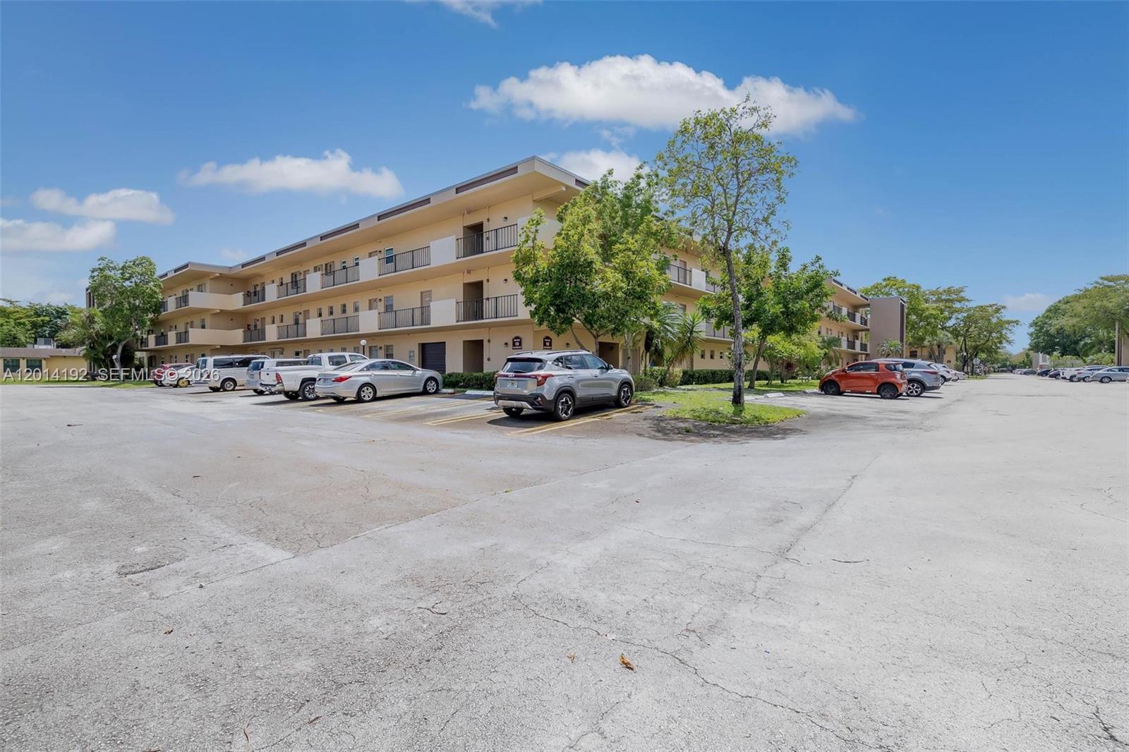 A multi-story apartment building features exterior balconies and a large parking lot in front — 100 Berkley Rd # 106, Hollywood FL 33024, HOLLYWOOD, FL