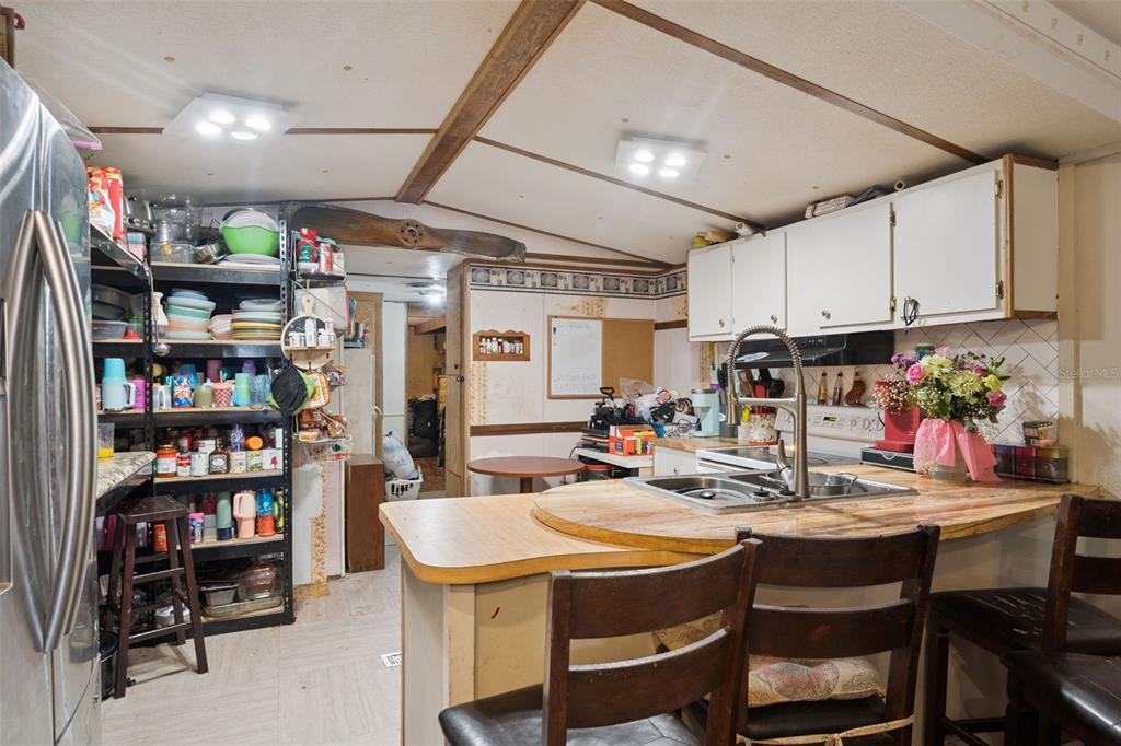 A kitchen with white cabinets, a stainless steel dishwasher, and a view into the living area — 10927 LUANA DRIVE, LEESBURG, FL