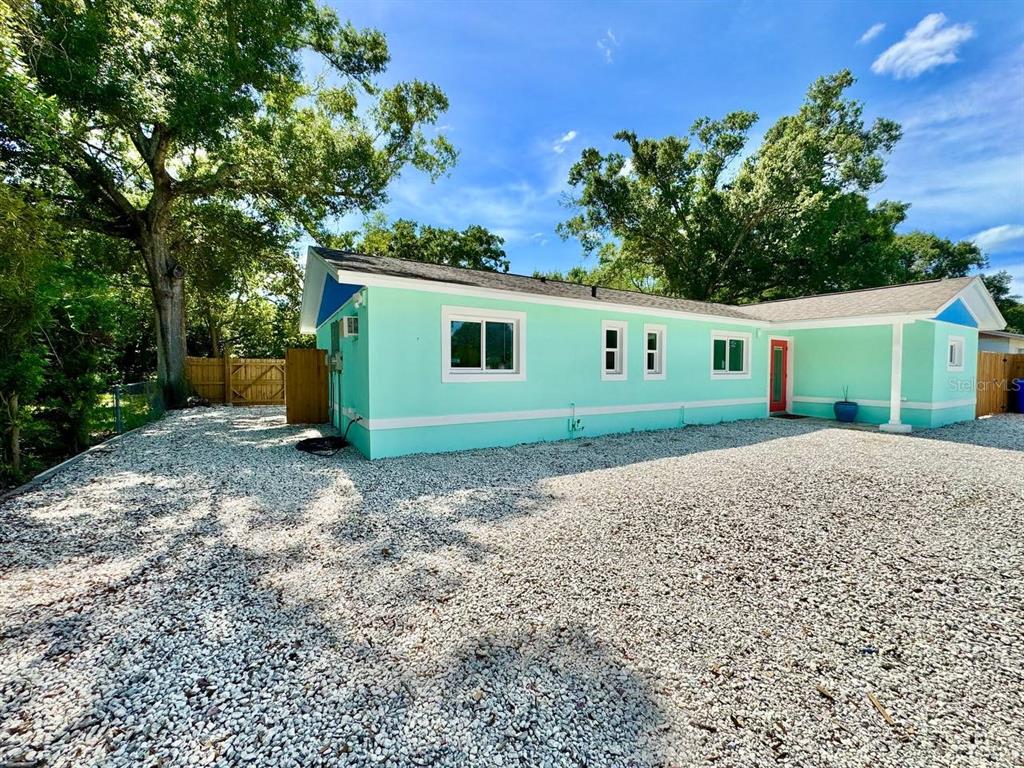 A light green house with a gravel driveway and large trees under a blue sky — 4306 PORPOISE DRIVE UNIT A, TAMPA, FL