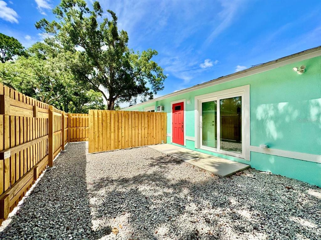 A backyard with a gravel ground, a wooden privacy fence, and a mint-colored exterior wall — 4306 PORPOISE DRIVE UNIT A, TAMPA, FL