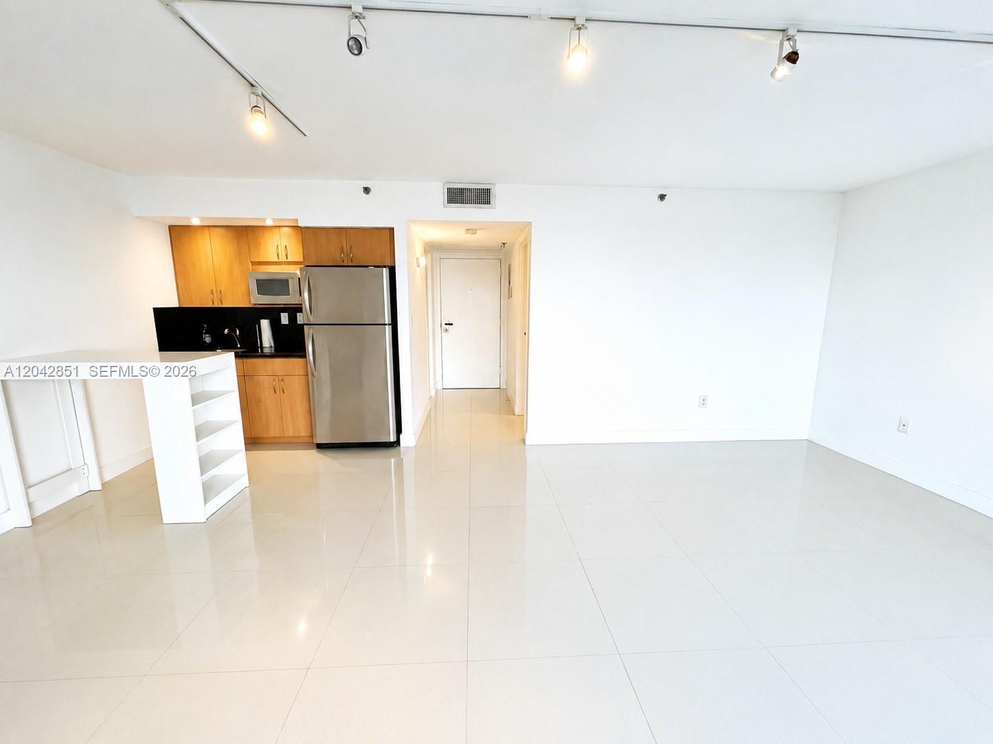 A kitchen with wood cabinets and stainless steel appliances opens into a white-tiled living area — 555 NE 15th St # 403, Miami FL 33132, MIAMI, FL