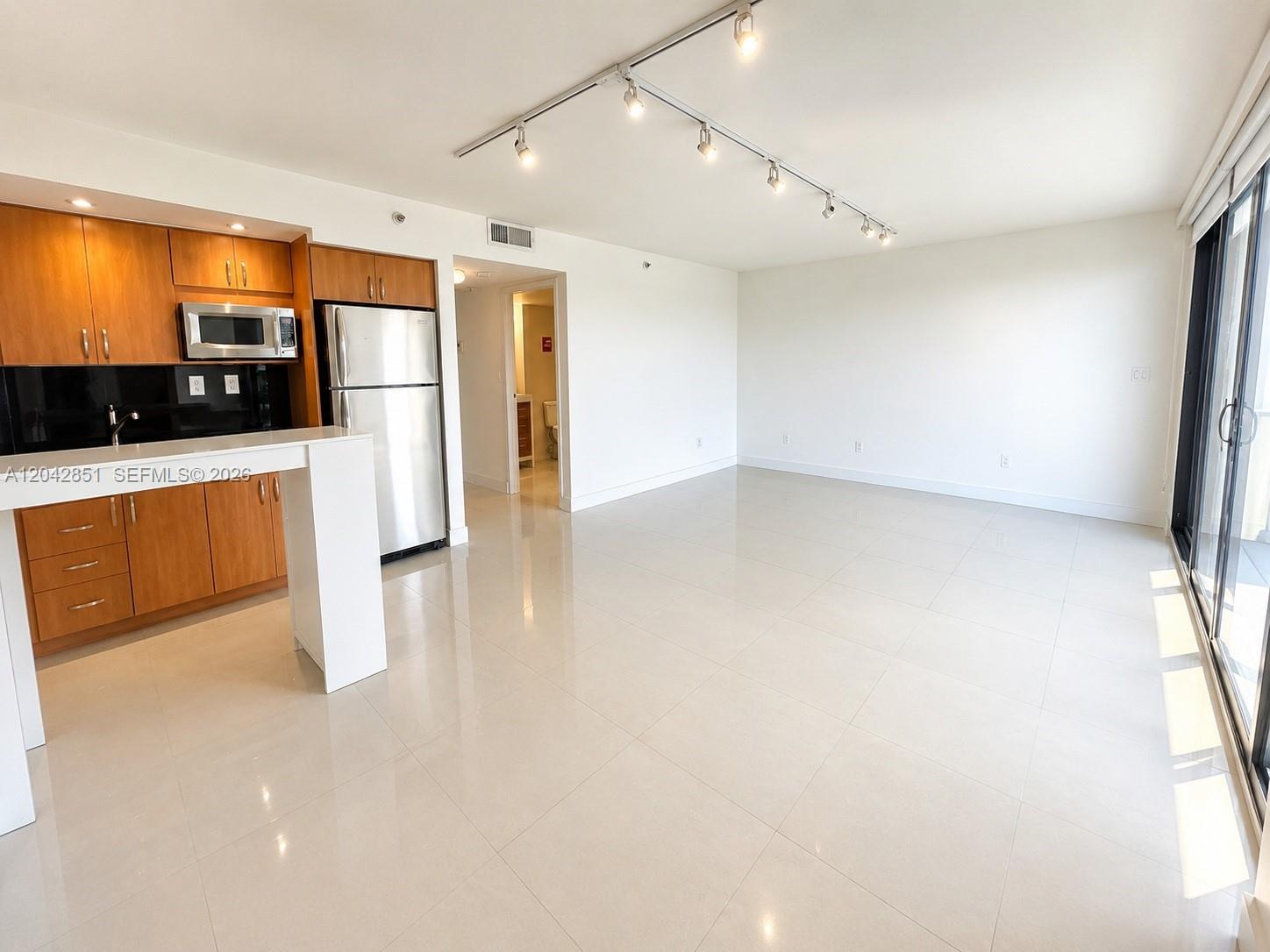 An open-concept kitchen with wood cabinets and stainless steel appliances overlooks a tiled living area — 555 NE 15th St # 403, Miami FL 33132, MIAMI, FL