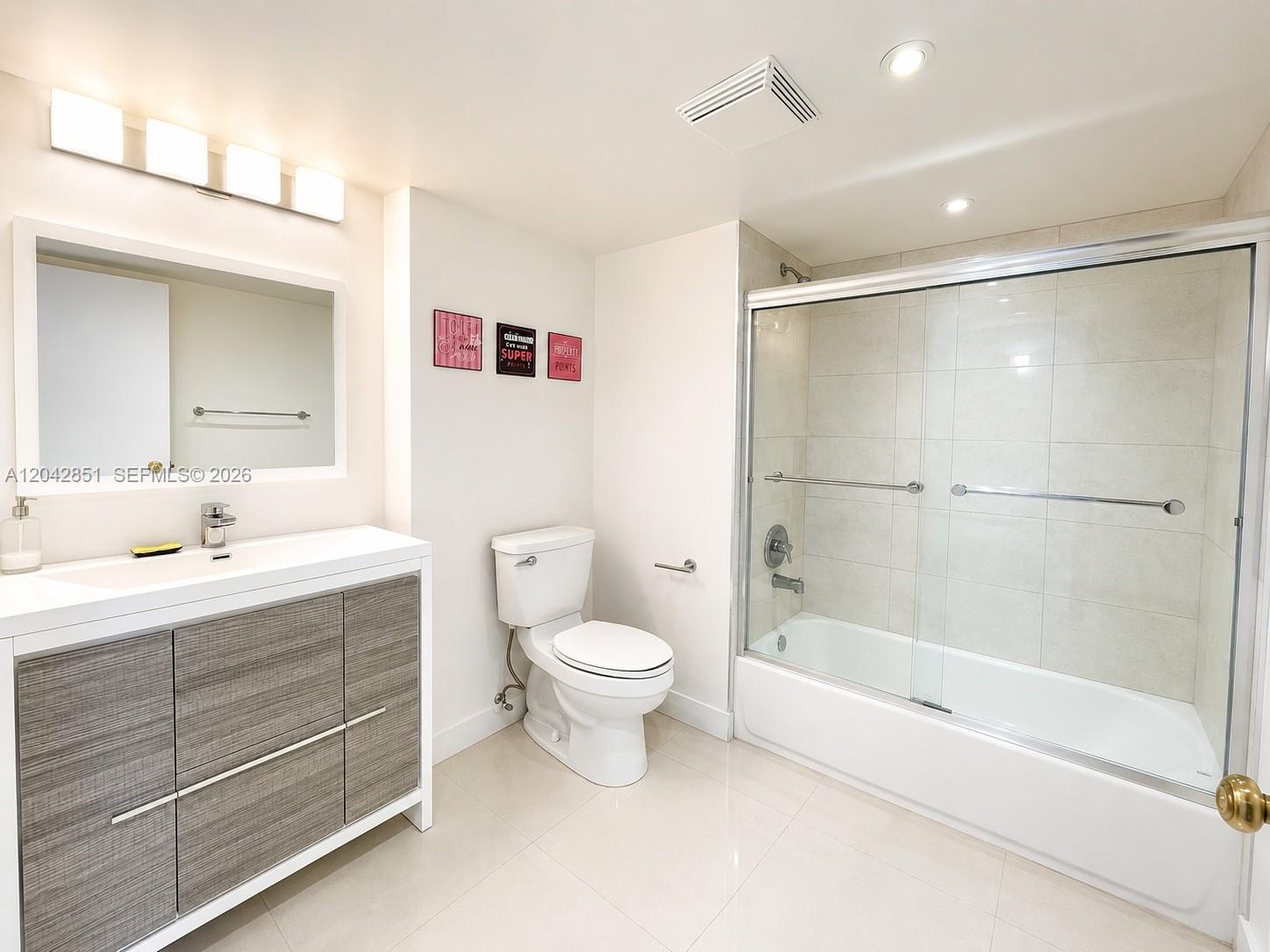 A bathroom features a wood-grain vanity, a white toilet, and a glass-enclosed bathtub shower — 555 NE 15th St # 403, Miami FL 33132, MIAMI, FL