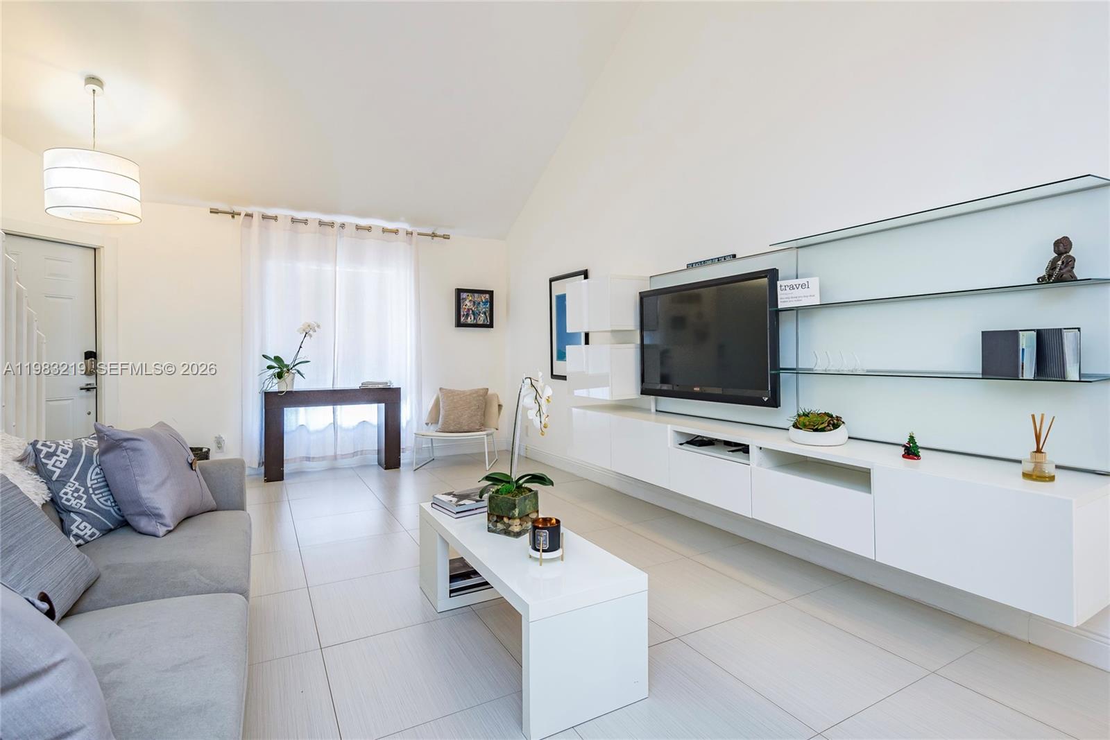 A modern living room features a gray sofa, white media console, and large glass shelving — 370 SE 2nd Ave # G3, Deerfield Beach FL 33441, DEERFIELD BEACH, FL