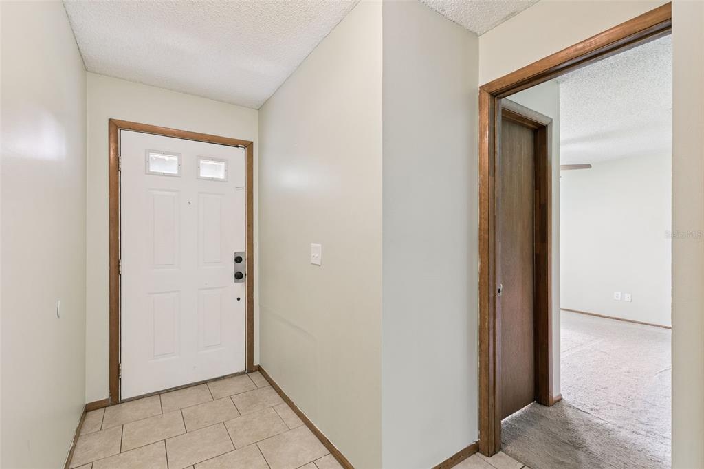 An entryway with a white front door, tile flooring, and a doorway leading to carpeted rooms — 3455 JUJUBE DRIVE, ORLANDO, FL