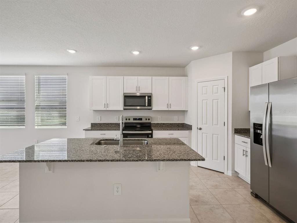 A kitchen with white cabinets, granite countertops, a center island, and stainless steel appliances — 3932 GIORGIO DRIVE, WINTER HAVEN, FL