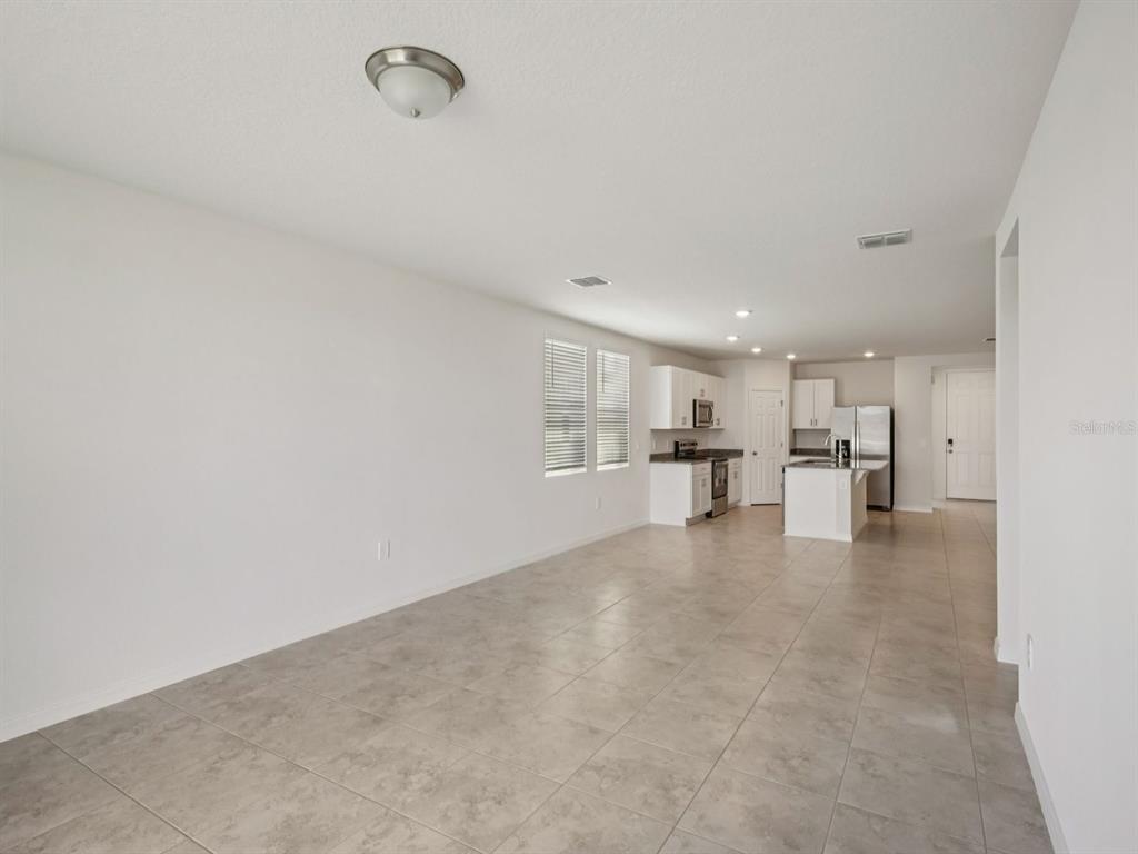 An open-concept room features light-colored tile flooring, white walls, and a kitchen in the background — 3932 GIORGIO DRIVE, WINTER HAVEN, FL