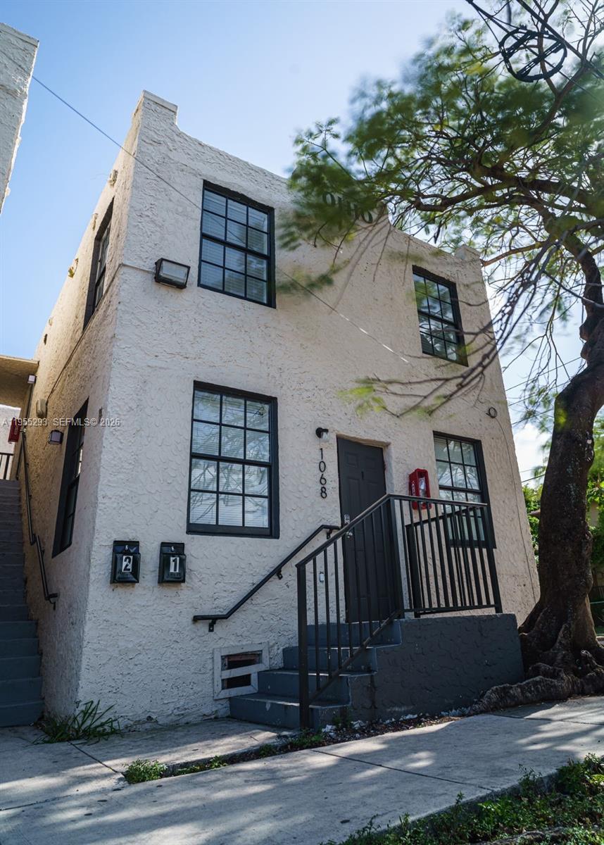 A two-story stucco building with dark-framed windows, a front staircase, and two mailboxes — 1068 NW 5th St, Miami FL 33128, MIAMI, FL