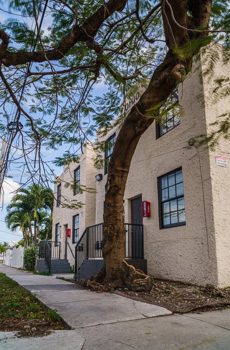 A two-story beige stucco building with black-framed windows stands behind a large tree — 1068 NW 5th St, Miami FL 33128, MIAMI, FL